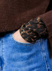 Een persoon met een blauwe spijkerbroek en de Omani Essential - Leopard bruine fuzzy sweater (stijl 0005856), met een manchet met luipaardprint, heeft zijn hand in de zak van zijn spijkerbroek gestoken.