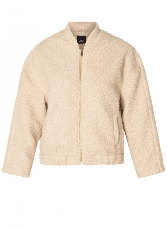 De Carmen-Maria is een crèmekleurig, getextureerd fleece teddylook jasje met een rits aan de voorkant, lange mouwen en twee steekzakken voor een comfortabele pasvorm - perfect voor het tussenseizoen. Afgebeeld op een effen witte achtergrond.