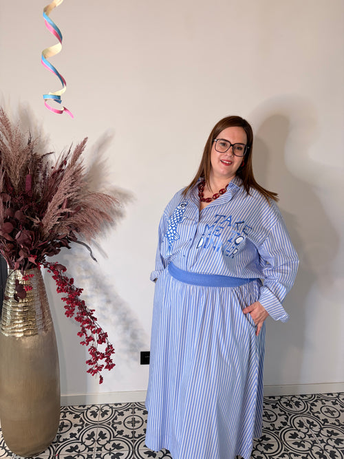 Dame draagt lichtblauwe gestreepte midi rok van Milano Italy met elastische tailleband, gecombineerd met een blauwe blouse.Dame draagt luxe lichtblauwe gestreepte blouse van Milano Italy met borduursels en elegante pasvorm.
