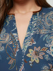 Close-up van een vrouw die de Bohemian blouse - Mat Fashion draagt, met een blauwe bloemen- en paisleyprint en een kleine inkeping in de halslijn. Haar haar, gedeeltelijk zichtbaar aan de linkerkant, complementeert de bohostijl.