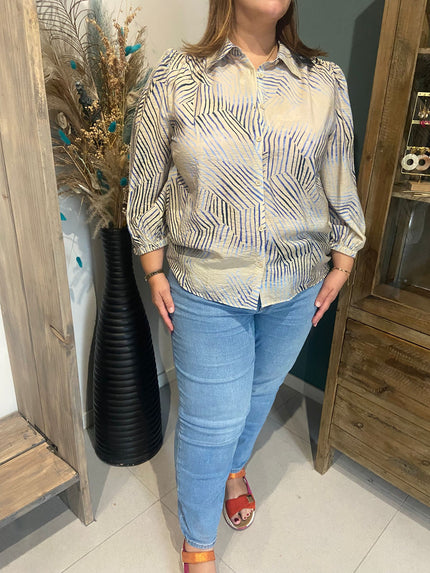 Een vrouw met een YEST Hemd in lichtblauwe strepen, een lichtblauwe spijkerbroek en rode sandalen staat binnen naast een hoge zwarte vaas met gedroogde bloemen en een houten kast. Haar hoofd is niet zichtbaar in het beeld.