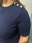 Een close-up van iemand die de Floortje - Dark Navy blouse draagt met drie decoratieve zilveren schouderknopen en een subtiele glittertextuur, waarbij het haar gedeeltelijk zichtbaar is.