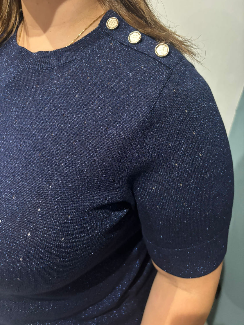 Een close-up van iemand die de Floortje - Dark Navy blouse draagt met drie decoratieve zilveren schouderknopen en een subtiele glittertextuur, waarbij het haar gedeeltelijk zichtbaar is.