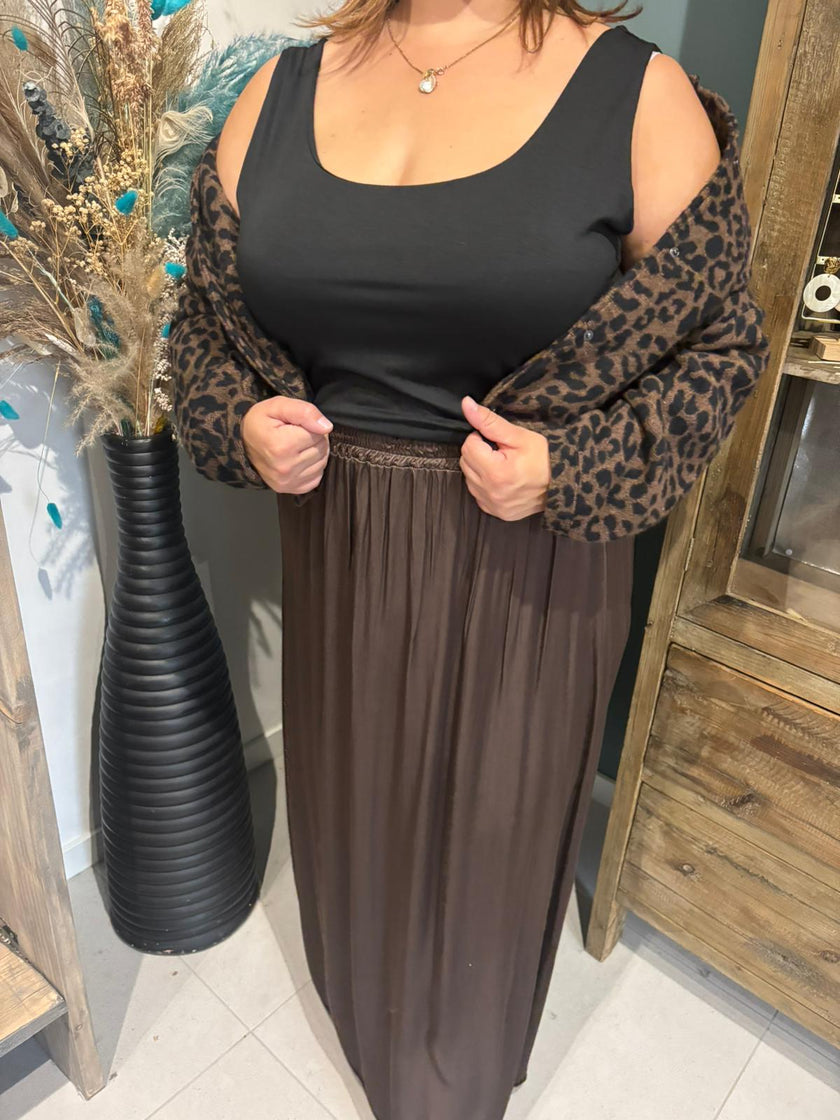 Een vrouw, haar gezicht niet te zien, draagt een Zwart topje, een bruine maxirok en een vest met luipaardprint (TU, One Size Mapping 48-54), staat binnen bij een hoge zwarte vaas met gedroogde bloemen en een houten kast.