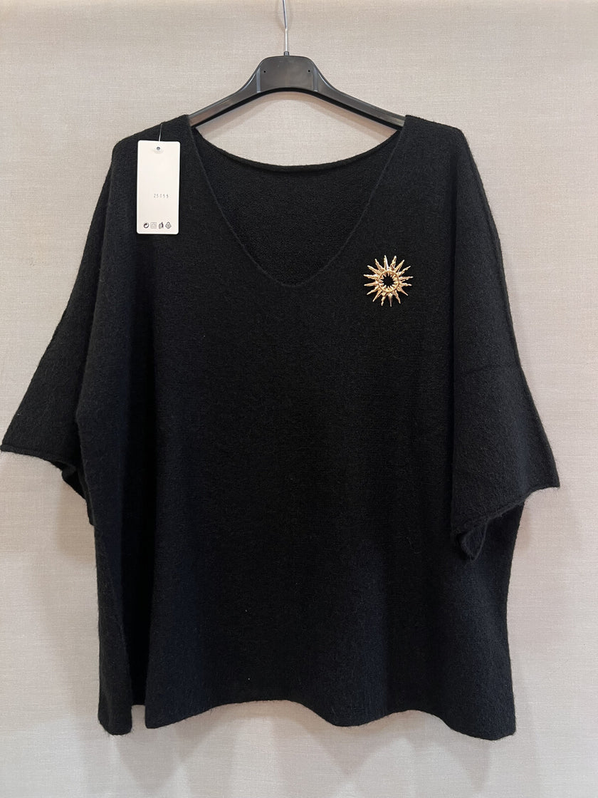 Een losvallende Trui - Zwart van Bourgondië met driekwart mouw en V-hals, op een hanger. Goudkleurige zon-broche op de borst, wit label op de schouder. Past maat 38-48. Ideaal voor herfst/winter 2025.