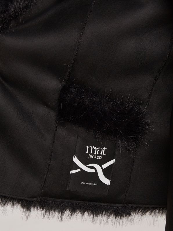 Close-up van een Zwarte bontjas van Mat Fashion, met een opgestikt myat Jackets-label boven een logo en de website van chosntwins-biz. De gladde stof en nette stiksels benadrukken de luxe van deze dubbelzijdige winterjas.